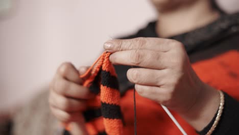 primer plano desde abajo de las manos de la mujer tejiendo una bufanda en color rojo y negro