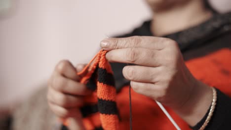 close up from below of woman's hands knitting a scarf in red and black color