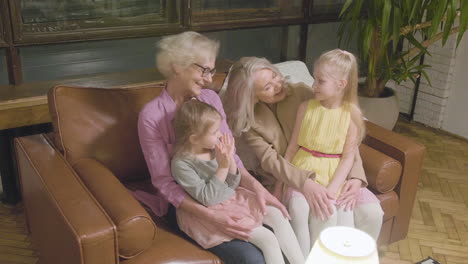 two grandmothers talking and spending time with their two granddaughter while sitting on sofa at home