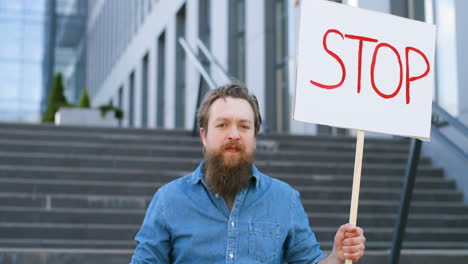 porträt eines bärtigen kaukasiers, der ein schild mit der haltestelle hält und auf der straße in die kamera schaut