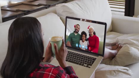 Mixed-race-woman-using-laptop-on-video-chat-with-family-during-christmas-at-home