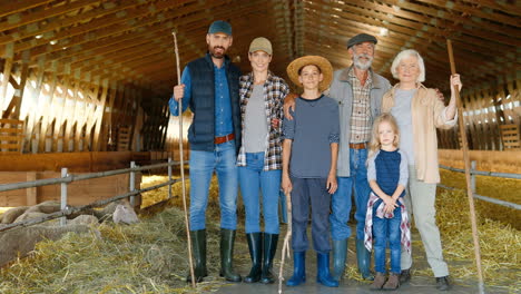 portrait of happy caucasian family of farmers standing in a stable with livestock and smiling to camera