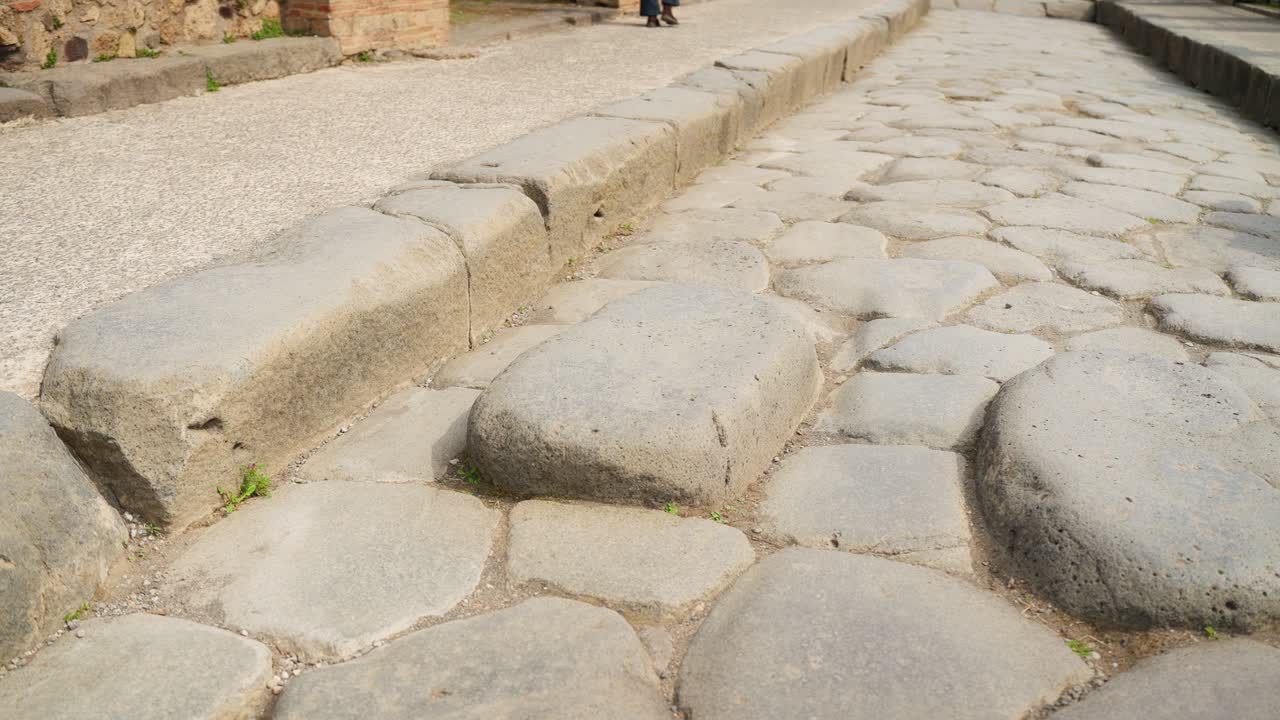 Close-up of an ancient Pompeii stone street with raised stepping stones and worn Roman paving, showing the preserved layout of the historic roadway in Italy