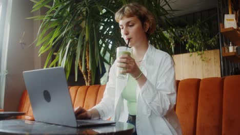 woman working on laptop in a cafe drinking a smoothie
