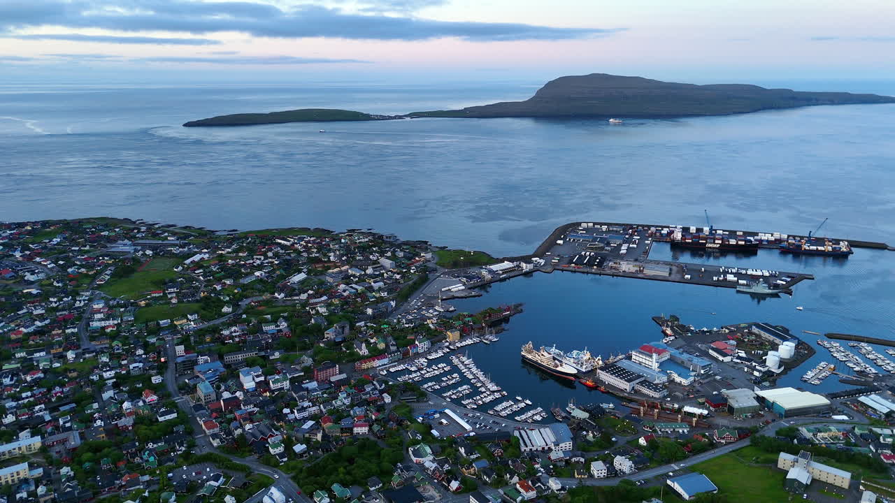 Cinematic aerial view of torshavn harbor in faroe islands with fishing boats, colorful houses, shipping port and dramatic coastline under soft evening light