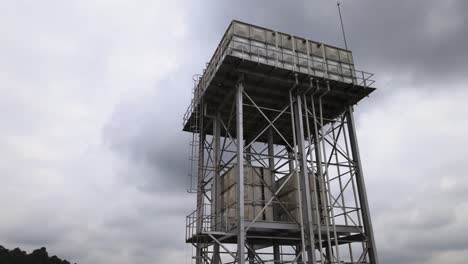 aerial establishing shot of a large water storage metallic structure with containers at a factory