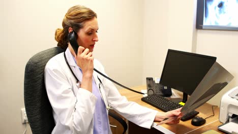 female doctor examining an x-ray while talking on telephone