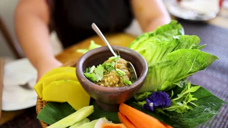a person presents a bamboo basket of roasted green chili dip and assorted fresh vegetables in bright natural light, highlighting northern thai cuisine and vibrant colors