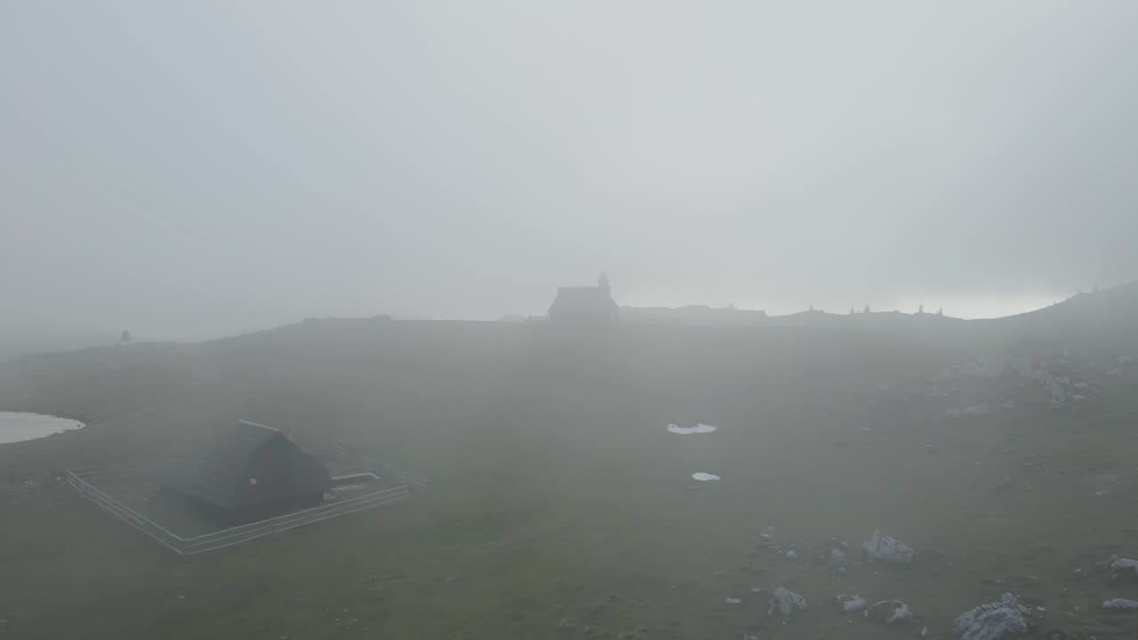 Flyfoto av tåkedekt kapell på en høyde med grønt gress, Velika Planina, Kamnik, Slovenia