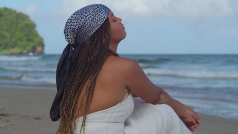 Left-pan-of-a-young-woman-at-the-beach-sitting-in-the-sand-enjoying-the-ocean-breeze