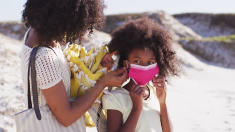 african american mother putting face masks on daughters face on the beach