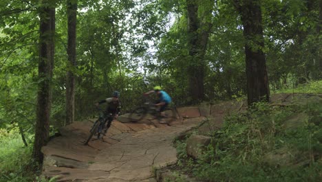 two people bicycling through a forest on a trail