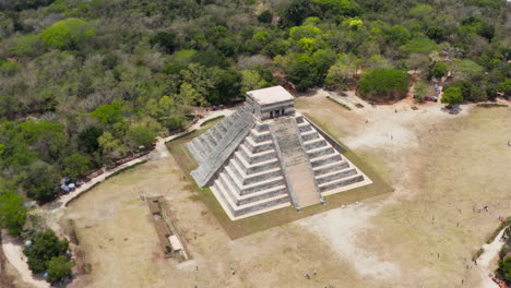 Aerial-pull-back-footage-of-old-Maya-town-site.-Big-stone-pyramid-of-temple-and-several-smaller-buildings.-Historical-monuments-of-pre-Columbian-era,-Chichen-Itza,-Mexico.