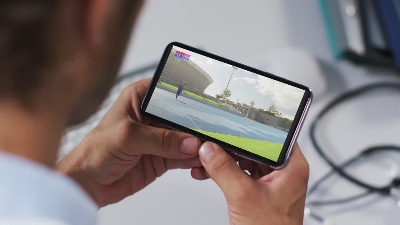 compuesto de un médico masculino viendo un evento de jabalina de atletismo en un teléfono inteligente