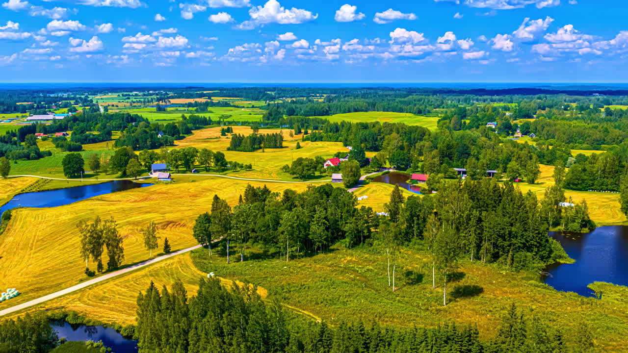 Picturesque ponds, farms, trees and fields of crops in a vibrant rural landscape in Europe under a fluffy cloudscape - aerial parallax hyper lapse