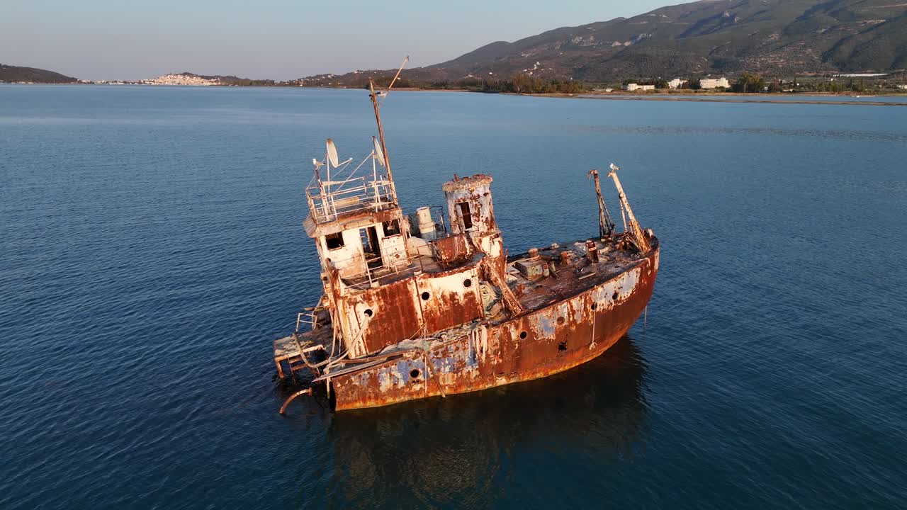 Peloponneso, Isola di Poros, Vista aerea all'indietro da una nave affondata arrugginita che giace tranquillamente su un mare calmo, con Poros e colline sullo sfondo