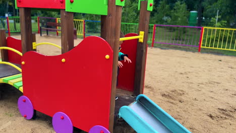 cute dark-haired toddler runs by the playground. smiling child slides down and runs by the playground.