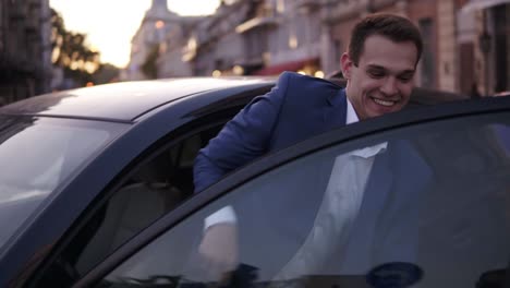 hombre apuesto y confiado en ropa formal azul salga del coche. joven hombre de negocios abre la puerta del coche y mirando a la cámara, sonriendo