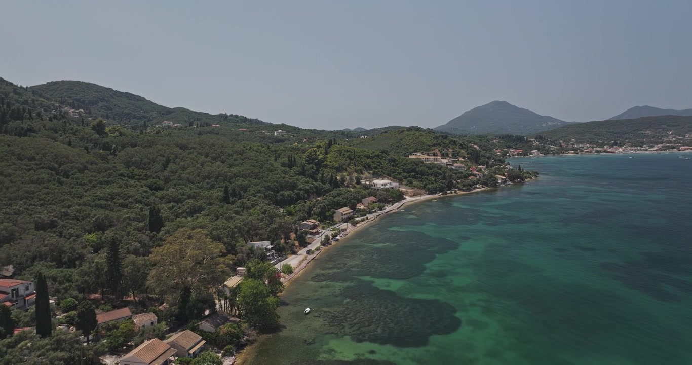Corfu Island Greece Aerial v2 flyover along Psaras and Mesongi, revealing a curved turquoise shoreline, forested hills and waterfront homes - Shot with Mavic 3 Pro Cine - July 16th 2024