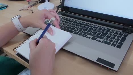 Writer drafting ideas in a notebook before typing on a laptop.