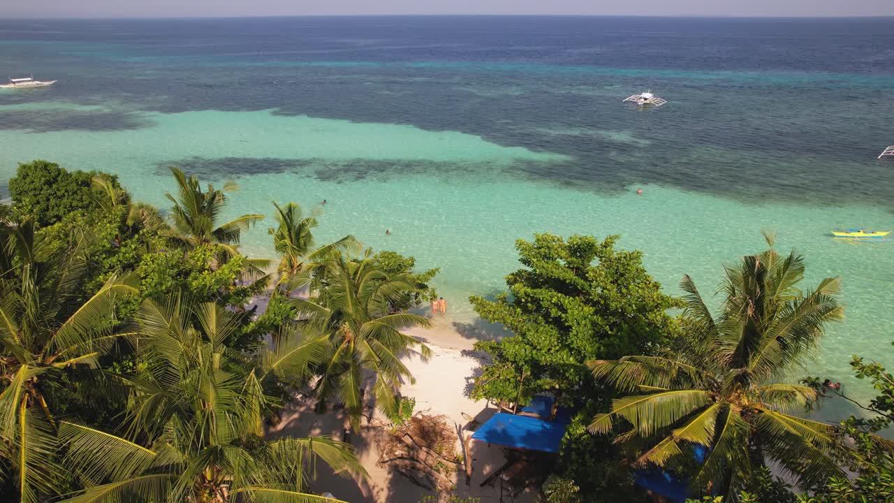Video drone 4K di una coppia che esce dall'oceano blu cristallino, verso la sabbia bianca a White Beach a Bohol, Filippine