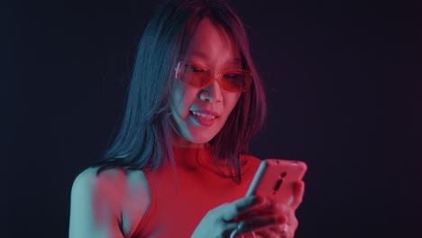 woman using a smartphone in a vibrant, neon-lit studio setting.