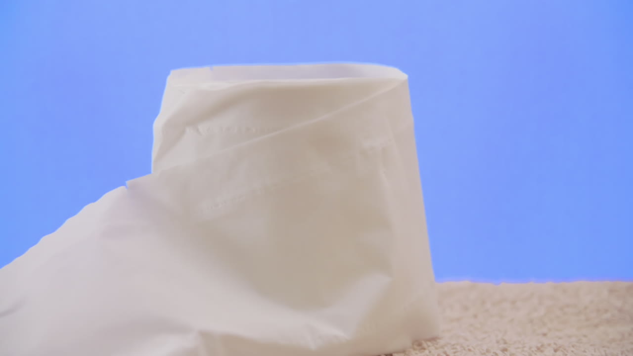 en el baño, recogiendo y dejando un rollo de papel higiénico, casi lleno y sin usar, dejado en una toalla, sobre un agradable fondo azul