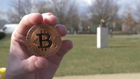 token bitcoing de cobre con la estatua de satoshi nakamoto en el fondo