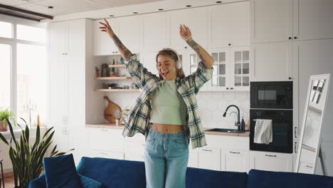 young happy lady wearing wireless headset listening to music and dancing on couch, slow motion