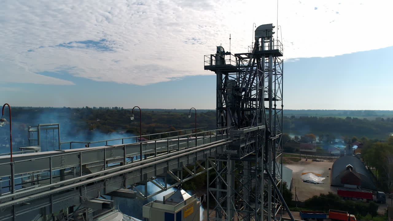 Top of industrial plant. Modern elevators and metal tower on nature background. Smoke goes from large factory in the countryside. Aerial view.