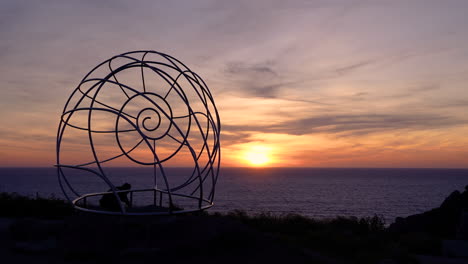 atemberaubender sonnenuntergang an der metallischen muschelschalenskulptur mit meereslandschaftshintergrund in cabo home, spanien