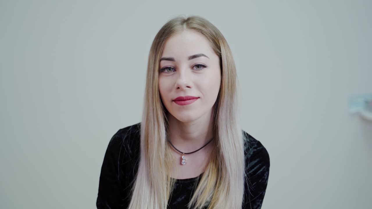 Beautiful blonde girl on white background sitting on white background smiling. Video in a studio.