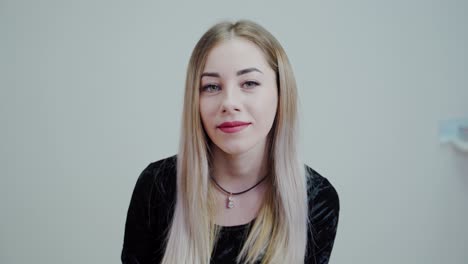 beautiful blonde girl on white background sitting on white background smiling. video in a studio.