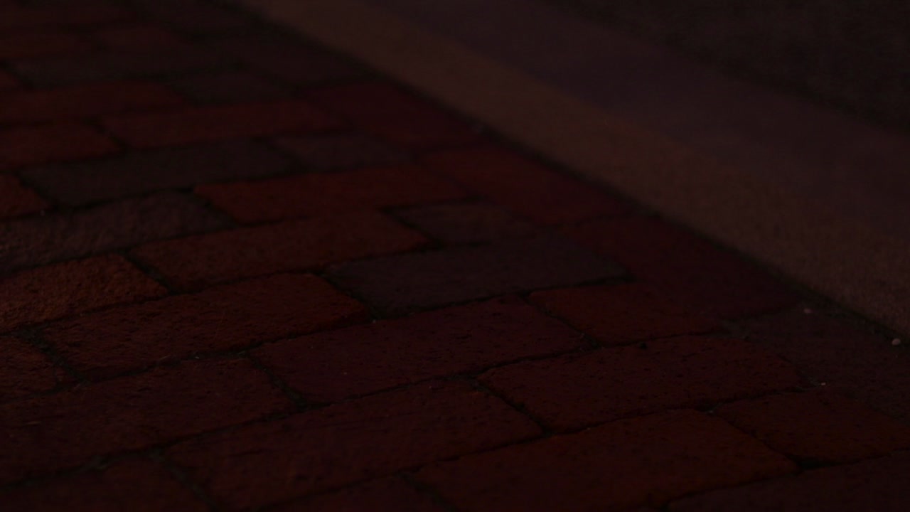Lights from passing cars shine over red brick sidewalk. Nighttime in the city.