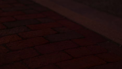lights from passing cars shine over red brick sidewalk. nighttime in the city.