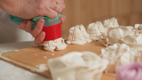 close up of caterer pressing piping bag with red nozzle as creamy dough drops onto parchment paper, forming delicate swirl designs for baking preparation in bright kitchen environment