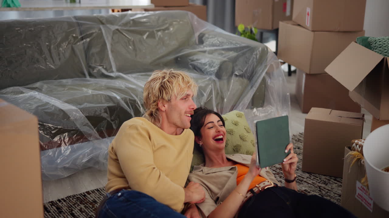 Happy Young Couple Laughing While Using Tablet in New Home