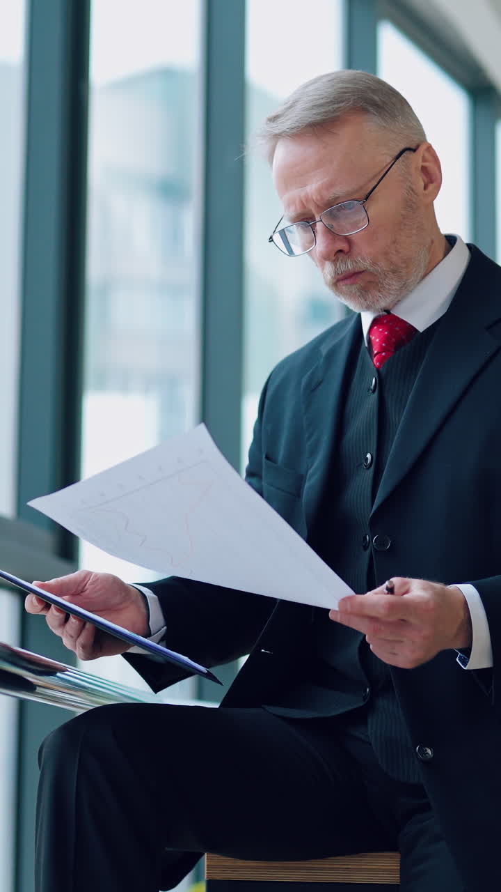 Portrait of mature man in cafe. Mature businessman sitting at coffee shop with documents. Vertical video
