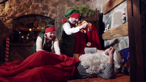 sleepy santa and elves. cheerful elves waking santa in his bedroom in special decorated room at christmas. santa getting from his bed at christmas night