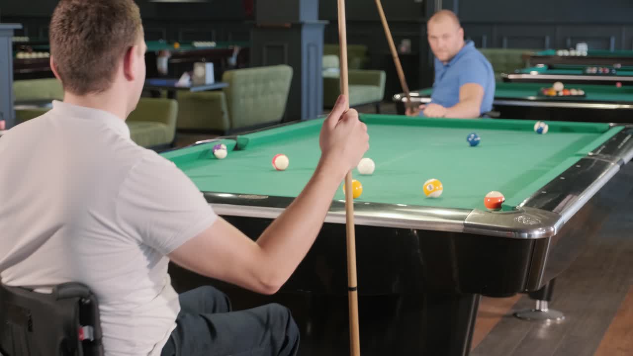 Adult men with disabilities in a wheelchair play billiards in the club
