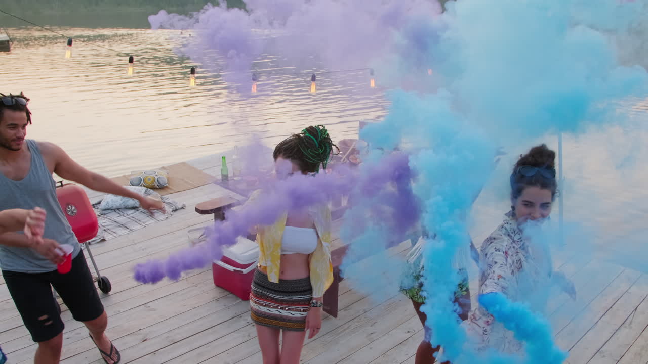 Jovens amigos despreocupados dançando no cais com bombas de fumaça coloridas