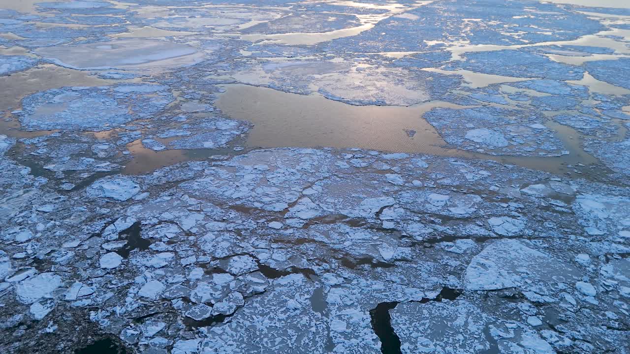 Andlöst vacker flygvy över Hudsonfloden, som visar en mosaik av isflak som glider ovanpå vattnet, belyst av varmt solljus. De intrikata ismönstren skapar en fantastisk visuell kontrast