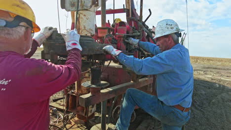 two mature men in protective helmets arranging equipment for oil boring. workers are at the truck for natural resources production.