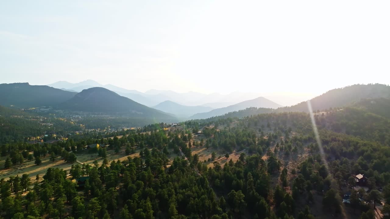 Drone high angle dolly of sunlit mountain range in Estes Park, autumn trees and scenic valley visible from high above
