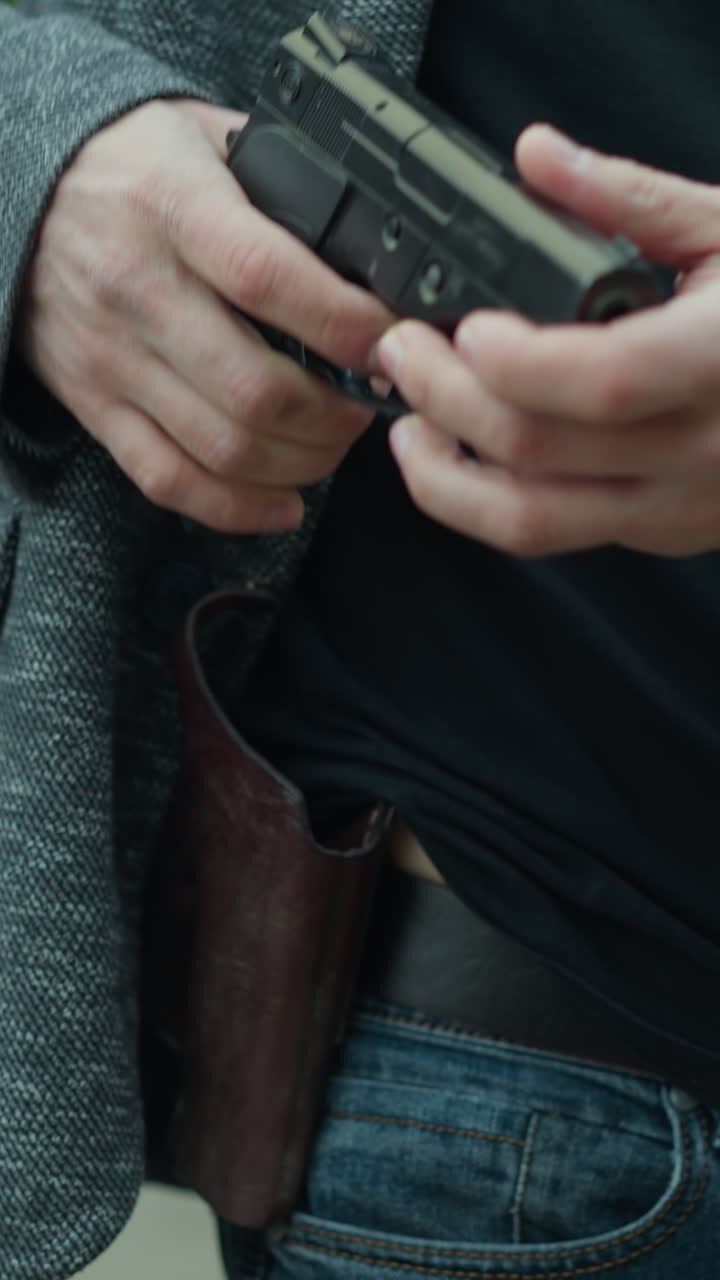 A close view of a man removing a concealed firearm under his jacket, standing beside a railway track, with blur forest view