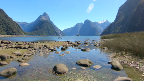 Tilt-up-from-a-close-shot-of-a-sandy-and-rocky-beach-to-a-wide-view-of-Mitre-Peak,-Milford-Sound,-New-Zealand