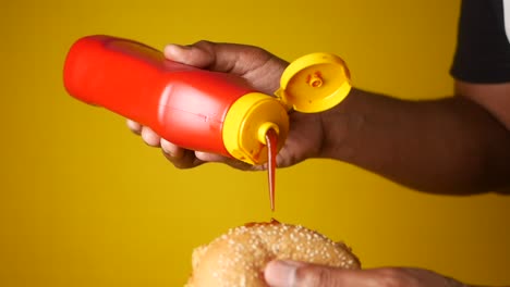 a hand squeezing ketchup onto a burger