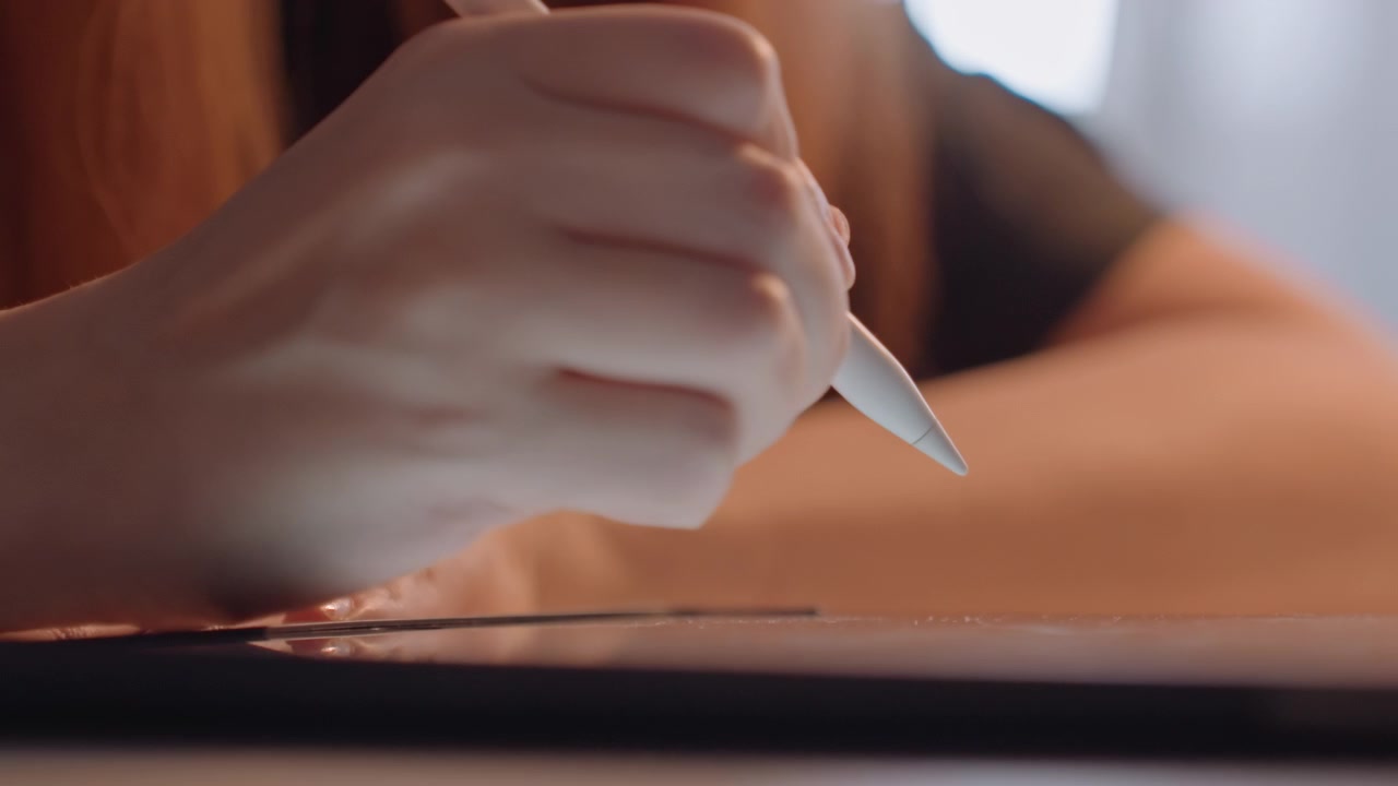 Close up of hand holding and moving white stylus. Interaction is continuous with visible lines being drawn. Background features warm tones and soft lighting suggesting indoor