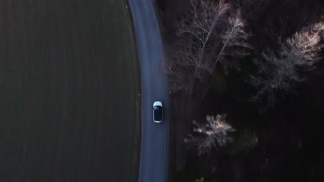 Top-down-Drone-Shot-of-a-Car-driving-on-a-lonely-Road-next-to-a-Forest