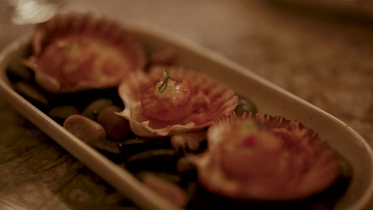 A chef arranges grilled scallops on a platter with precision under warm, ambient lighting